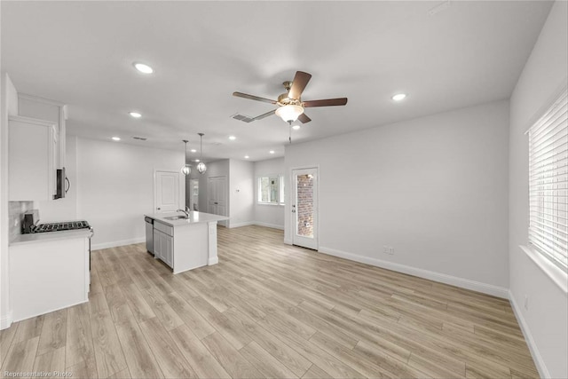 kitchen featuring white cabinets, light hardwood / wood-style floors, hanging light fixtures, and an island with sink