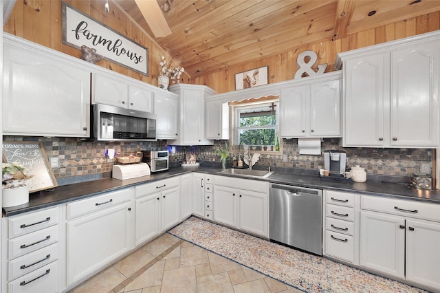 kitchen with backsplash, dark countertops, a sink, appliances with stainless steel finishes, and white cabinetry