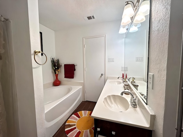 bathroom with hardwood / wood-style flooring, an inviting chandelier, a bathing tub, vanity, and a textured ceiling