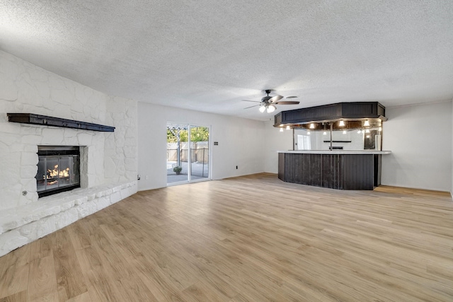 unfurnished living room featuring a textured ceiling, ceiling fan, light hardwood / wood-style floors, and a fireplace