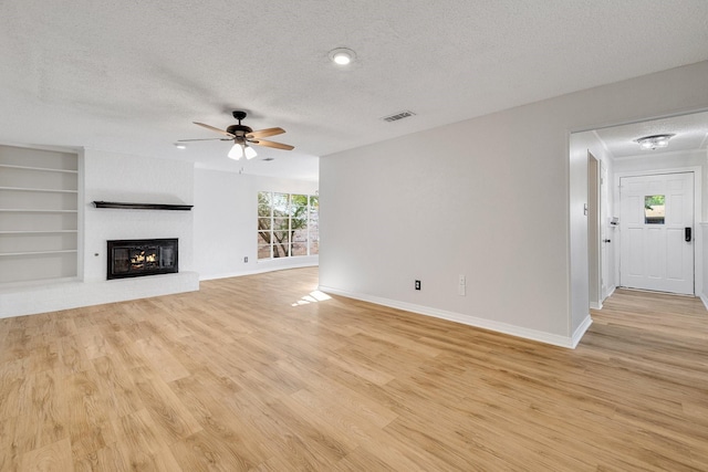 unfurnished living room featuring ceiling fan, built in features, a textured ceiling, and light wood-type flooring