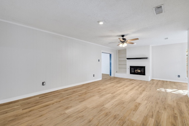 unfurnished living room featuring ornamental molding, ceiling fan, a textured ceiling, light wood-type flooring, and built in shelves