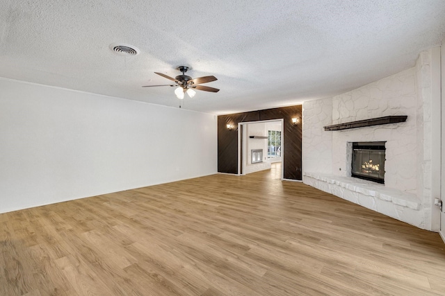 unfurnished living room featuring wooden walls, light hardwood / wood-style flooring, ceiling fan, a textured ceiling, and a fireplace