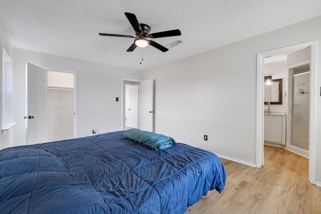 bedroom with a textured ceiling, light wood-type flooring, ensuite bathroom, and ceiling fan