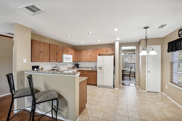 kitchen featuring kitchen peninsula, a breakfast bar, pendant lighting, light stone counters, and white appliances