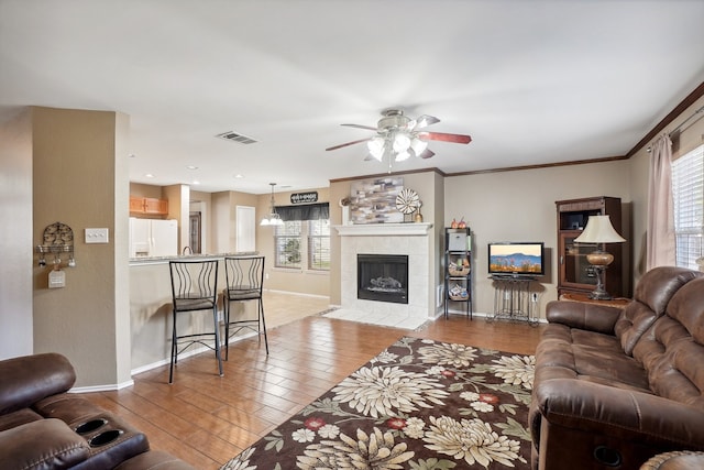 living room featuring ornamental molding, a tiled fireplace, light hardwood / wood-style floors, and ceiling fan