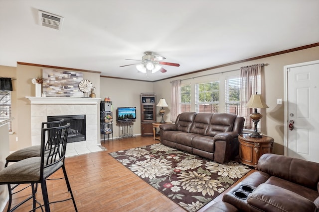 living room featuring ornamental molding, hardwood / wood-style floors, a tiled fireplace, and ceiling fan