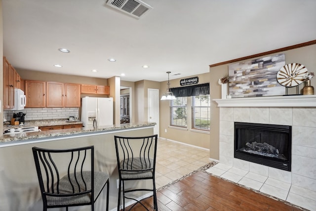 kitchen featuring white appliances, light hardwood / wood-style floors, a tiled fireplace, light stone counters, and decorative backsplash