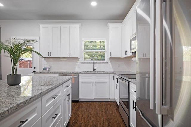 kitchen with light stone countertops, appliances with stainless steel finishes, sink, white cabinetry, and dark wood-type flooring