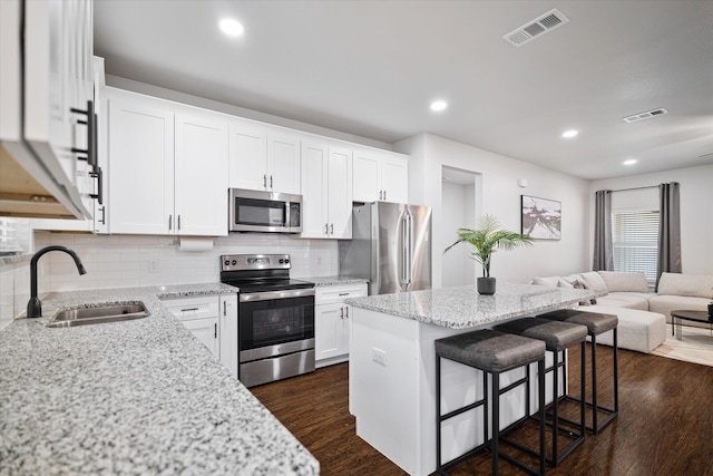 kitchen featuring white cabinets, a kitchen island, appliances with stainless steel finishes, light stone countertops, and sink