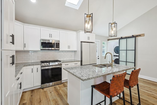 kitchen featuring stacked washer / dryer, a barn door, sink, vaulted ceiling with skylight, and stainless steel appliances