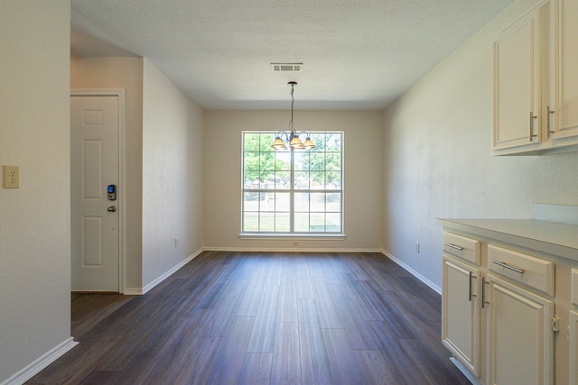 unfurnished dining area with a notable chandelier, dark hardwood / wood-style floors, and a textured ceiling