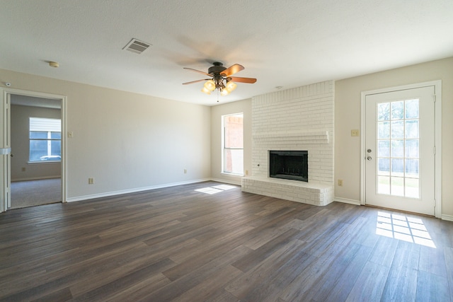 unfurnished living room featuring a brick fireplace, dark hardwood / wood-style floors, and a wealth of natural light