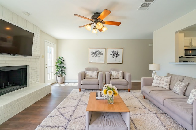 living room featuring ceiling fan, a brick fireplace, and dark hardwood / wood-style flooring