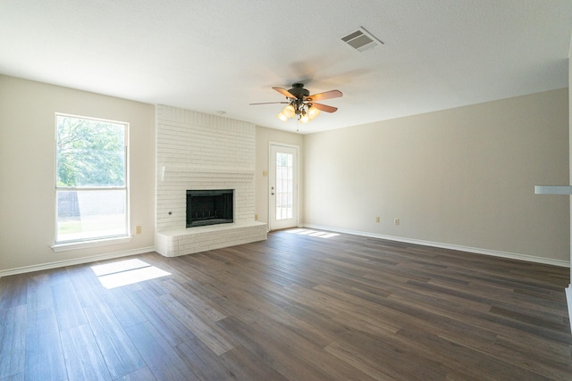 unfurnished living room featuring a brick fireplace, baseboards, dark wood-type flooring, and a ceiling fan