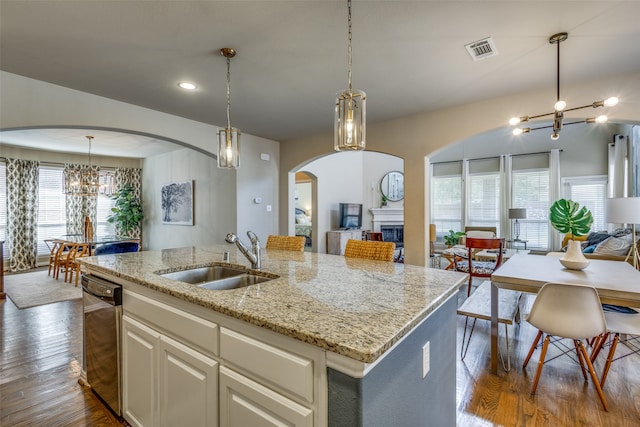 kitchen featuring hanging light fixtures, an island with sink, light stone countertops, dark hardwood / wood-style floors, and sink