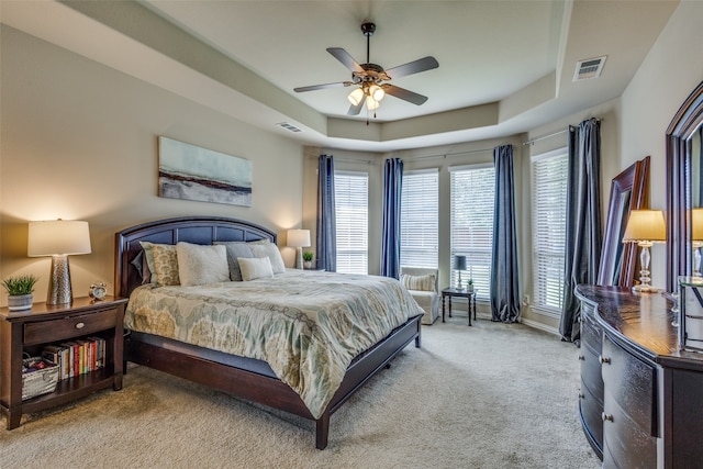 bedroom featuring a raised ceiling, light colored carpet, and ceiling fan