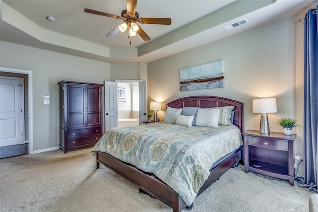 carpeted bedroom featuring ensuite bathroom, a raised ceiling, and ceiling fan