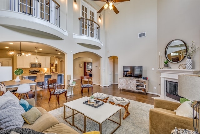 living room with dark hardwood / wood-style floors, ceiling fan with notable chandelier, and a high ceiling