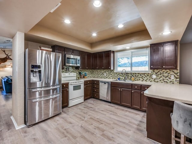 kitchen featuring stainless steel appliances, a tray ceiling, a sink, light countertops, and dark brown cabinetry