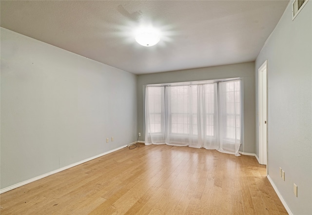 spare room with visible vents, a textured ceiling, light wood-style flooring, and baseboards