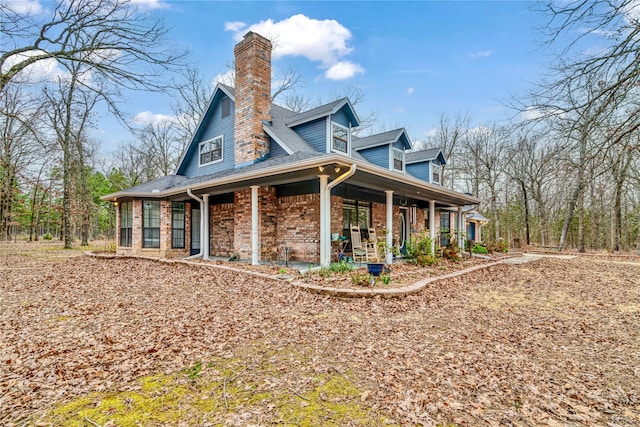 exterior space featuring a shingled roof, covered porch, brick siding, and a chimney