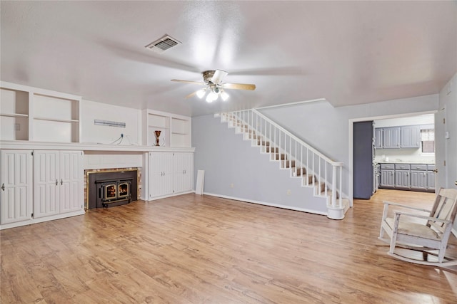 unfurnished living room with visible vents, a wood stove, ceiling fan, light wood-type flooring, and stairs