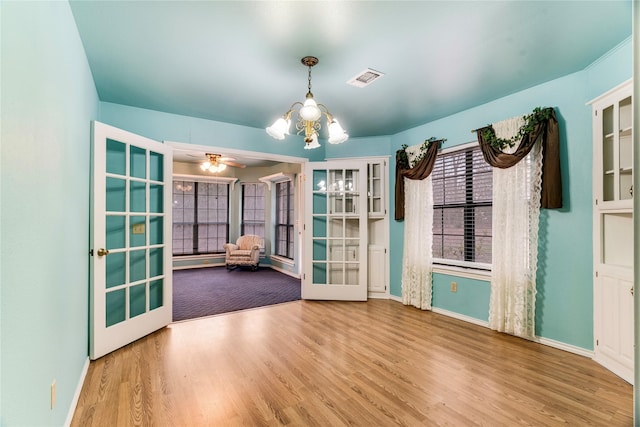 spare room featuring ceiling fan with notable chandelier, visible vents, wood finished floors, and french doors