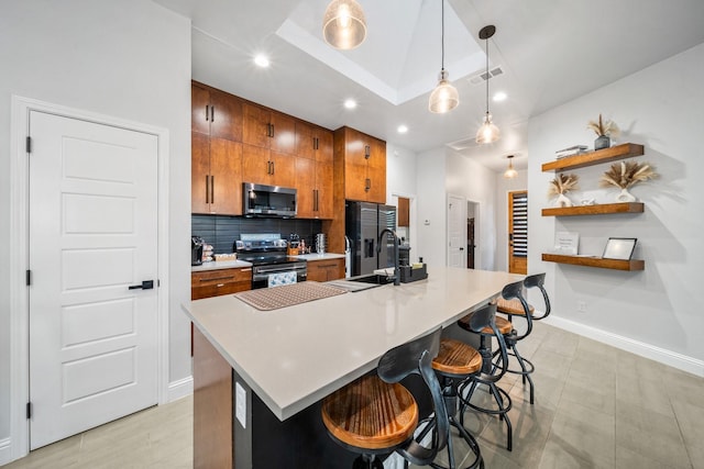 kitchen with appliances with stainless steel finishes, hanging light fixtures, a kitchen breakfast bar, and an island with sink