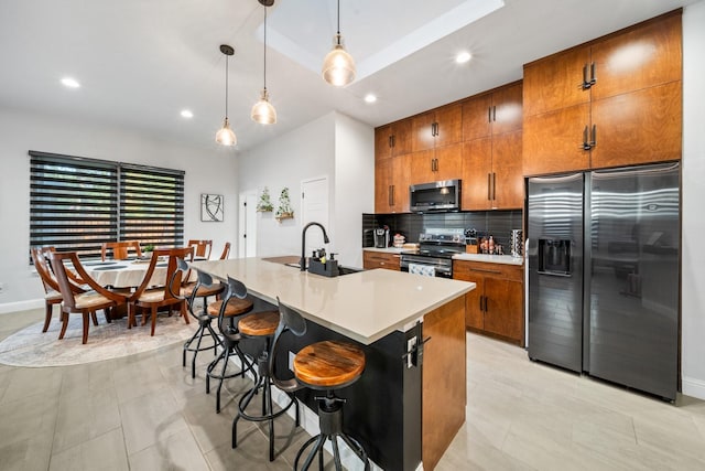 kitchen with a kitchen bar, stainless steel appliances, a kitchen island with sink, sink, and pendant lighting