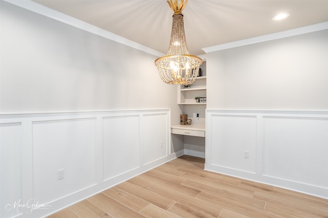 unfurnished dining area featuring light hardwood / wood-style floors, built in desk, crown molding, and an inviting chandelier