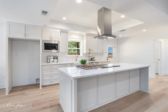 kitchen with white cabinets, a kitchen island, built in microwave, and light hardwood / wood-style flooring