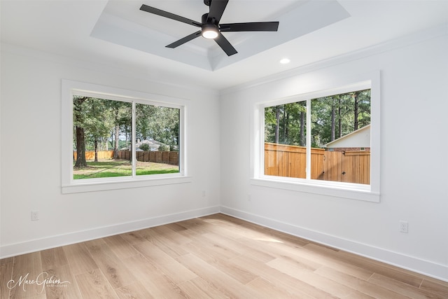 spare room featuring ceiling fan, a healthy amount of sunlight, a raised ceiling, and light hardwood / wood-style flooring