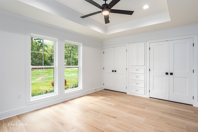 unfurnished bedroom featuring a raised ceiling, multiple closets, ceiling fan, and light hardwood / wood-style flooring