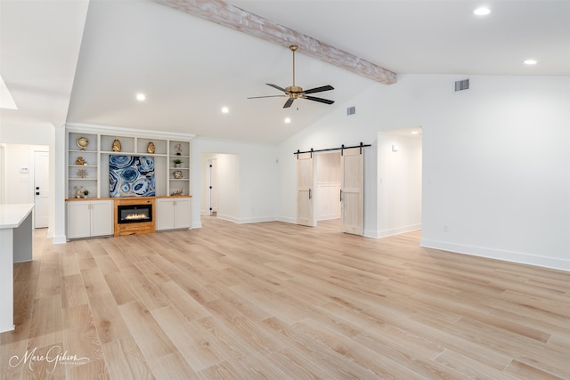 unfurnished living room featuring lofted ceiling with beams, light hardwood / wood-style floors, a barn door, and ceiling fan