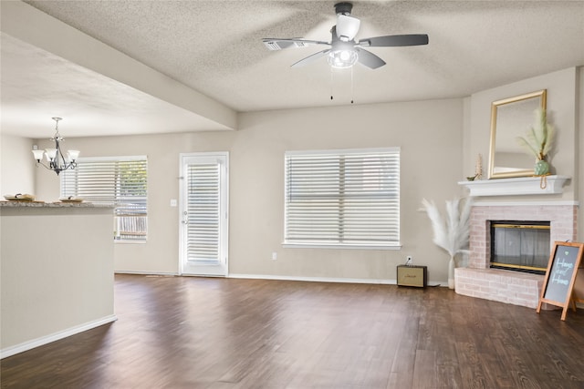 unfurnished living room featuring dark wood-style floors, a brick fireplace, a textured ceiling, baseboards, and ceiling fan with notable chandelier