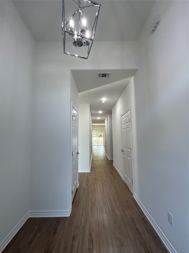 hallway with dark wood-type flooring and an inviting chandelier