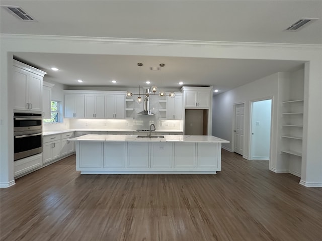 kitchen featuring white cabinetry, a center island, wall chimney exhaust hood, dark wood-type flooring, and pendant lighting