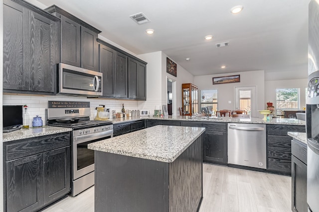 kitchen with appliances with stainless steel finishes, sink, decorative backsplash, a center island, and kitchen peninsula