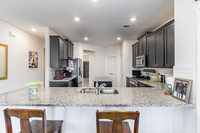 kitchen with appliances with stainless steel finishes, a breakfast bar, sink, kitchen peninsula, and light stone countertops