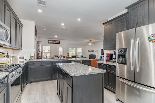 kitchen featuring appliances with stainless steel finishes, decorative backsplash, a center island, ceiling fan, and light stone countertops