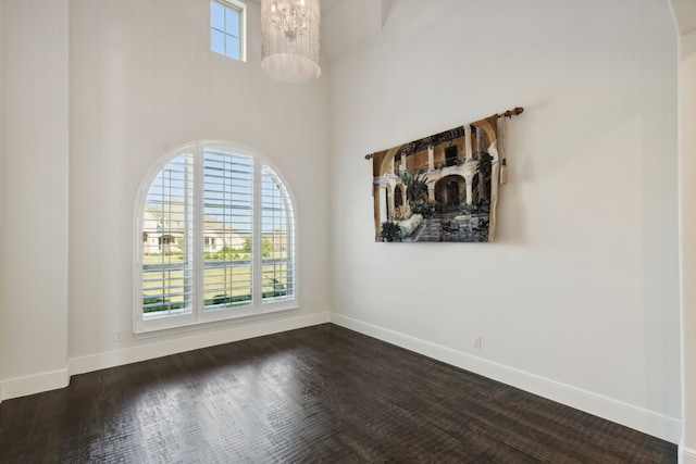 unfurnished room featuring a towering ceiling, dark wood-type flooring, and a healthy amount of sunlight