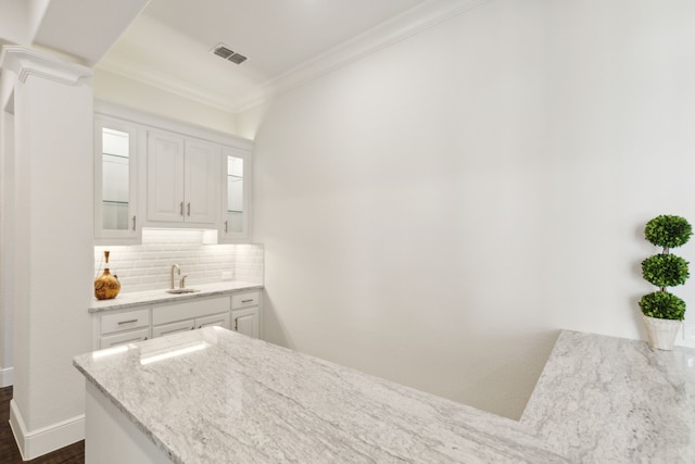 kitchen with ornamental molding, white cabinets, light stone counters, decorative backsplash, and dark hardwood / wood-style floors