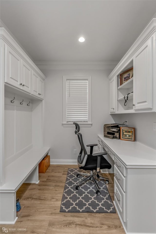 office space with crown molding, built in desk, and light hardwood / wood-style flooring