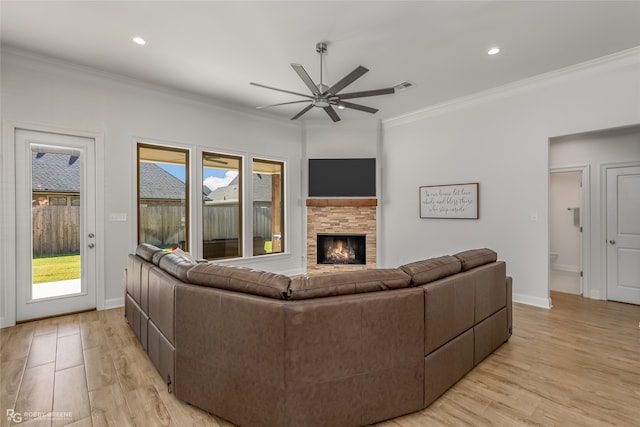 living room featuring ornamental molding, a stone fireplace, ceiling fan, and light hardwood / wood-style flooring