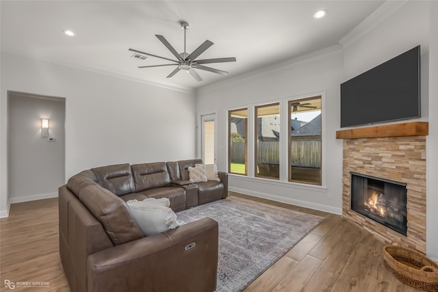 living room featuring crown molding, a fireplace, ceiling fan, and light wood-type flooring