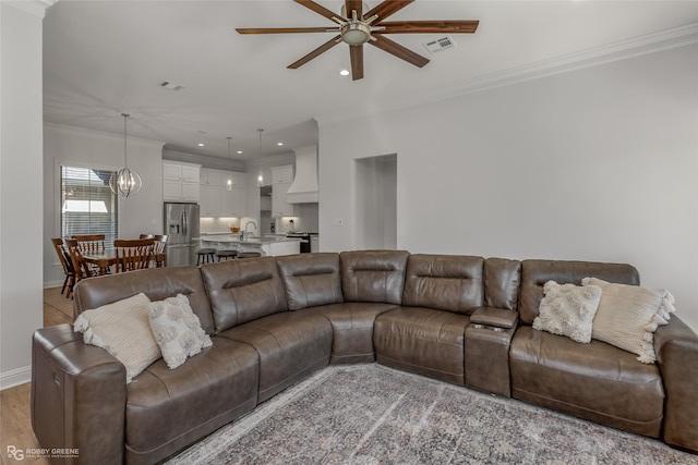 living room featuring sink, crown molding, ceiling fan with notable chandelier, and light hardwood / wood-style floors