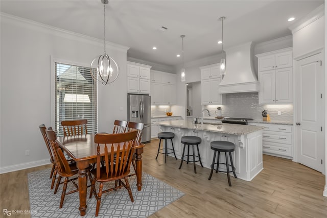 dining space featuring sink, crown molding, a chandelier, and light wood-type flooring