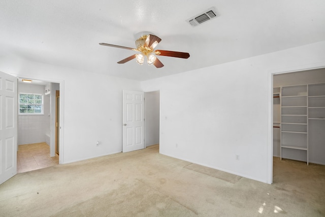 unfurnished bedroom featuring a closet, light carpet, a walk in closet, ensuite bathroom, and ceiling fan