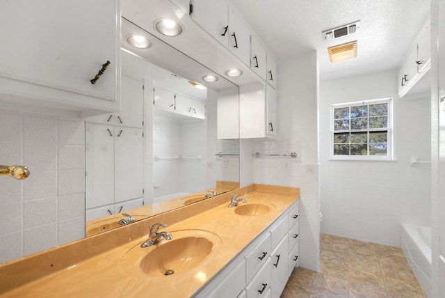 bathroom with tile walls, vanity, a textured ceiling, and a washtub